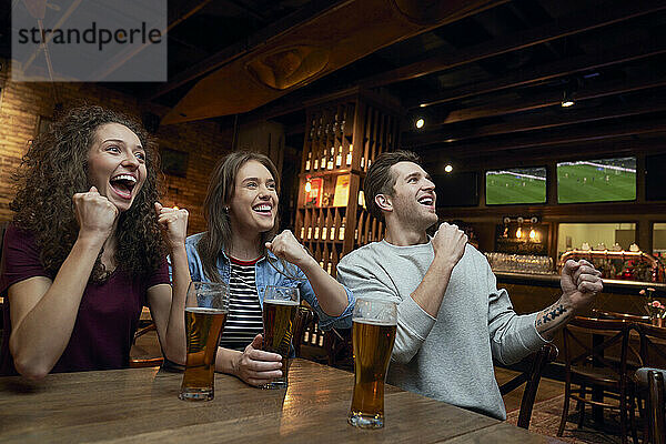 Fröhliche Fußballfans trinken Bier und schauen sich gemeinsam ein Spiel in einer Kneipe an