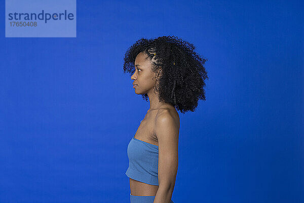 Junge Frau mit Afro-Frisur steht vor blauem Hintergrund