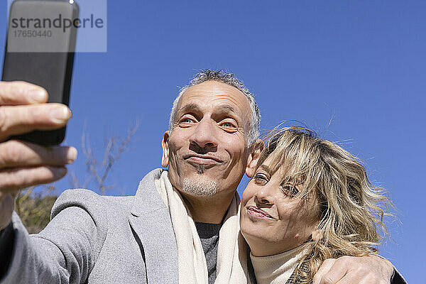 Mature couple taking selfie on smart phone in front of blue sky