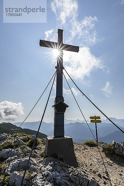 Gipfelkreuz unter bewölktem Himmel an einem sonnigen Tag