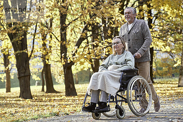 Älterer Mann geht mit behinderter Frau im Rollstuhl im Park spazieren