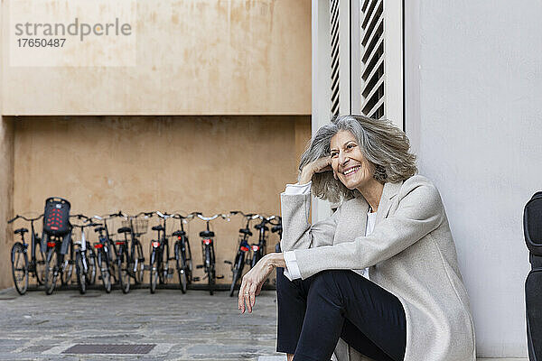 Glückliche ältere Frau mit grauen Haaren sitzt vor der Wand