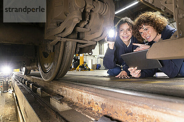 Ingenieur hält Tablet-PC in der Hand und analysiert Einschienenbahnrad mit Auszubildender in der Fabrik