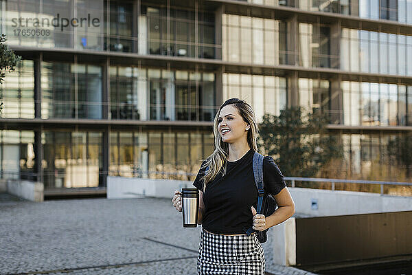 Lächelnde Geschäftsfrau mit isolierter Kaffeetasse auf Fußweg