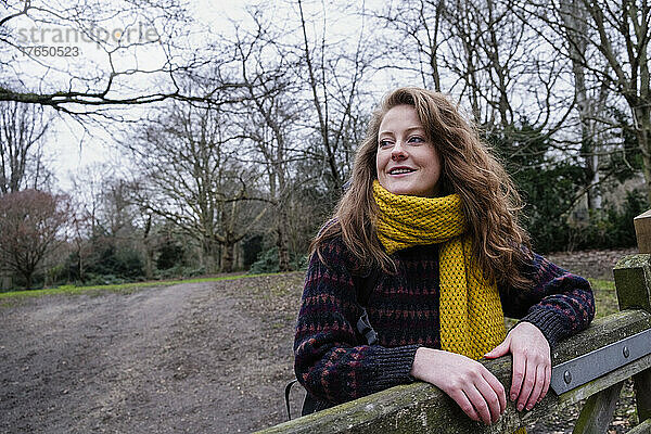 Lächelnde junge Frau mit gelbem Schal steht am Tor im Wald