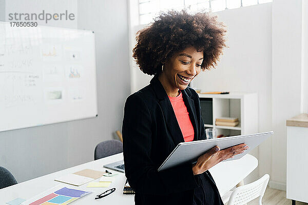 Glückliche junge Geschäftsfrau mit Afro-Frisur mit Tablet-PC im Büro
