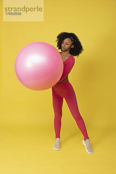 Junge Frau hält einen rosa Luftballon vor gelbem Hintergrund