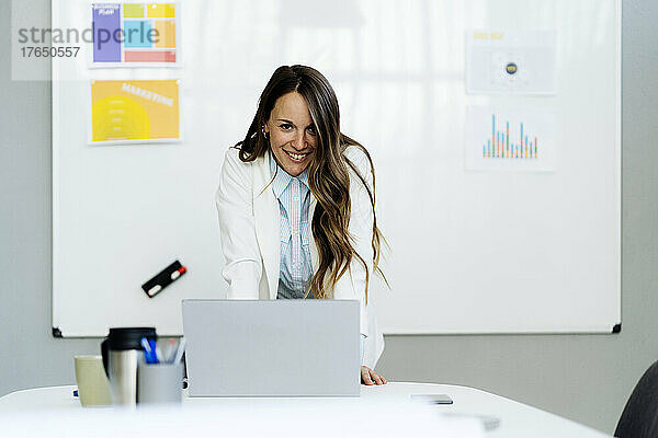 Glückliche Geschäftsfrau mit Laptop am Schreibtisch im Büro