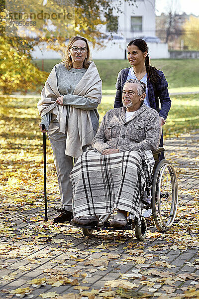 Ältere Frau spricht mit Krankenschwester und behindertem Mann  der im Rollstuhl im Park sitzt