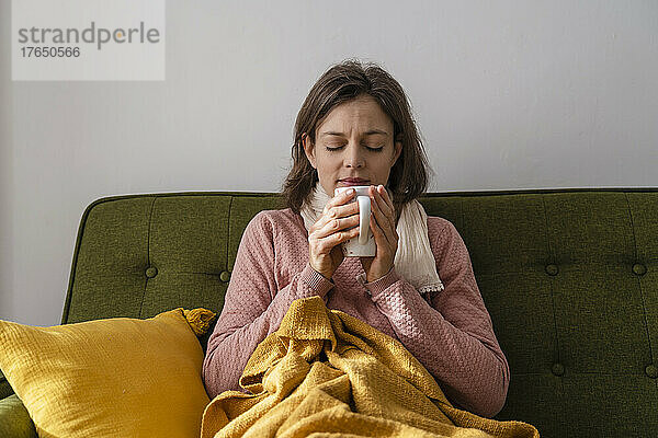 Kranke Frau mit Teetasse sitzt zu Hause auf dem Sofa