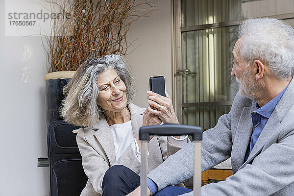 Lächelnde ältere Frau fotografiert Mann mit Mobiltelefon