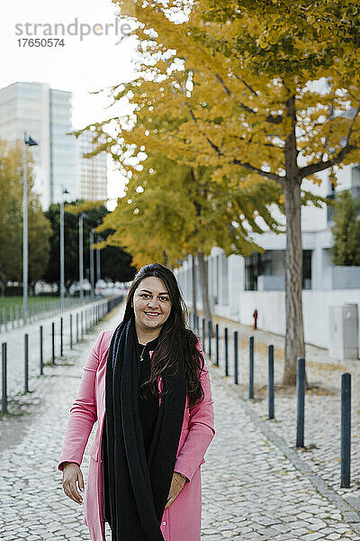 Lächelnde Frau steht auf dem Bürgersteig im öffentlichen Park