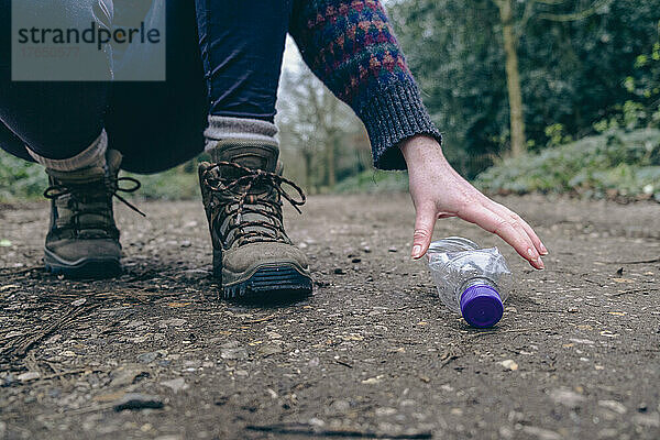 Junge Frau hebt Plastikflasche im Wald auf