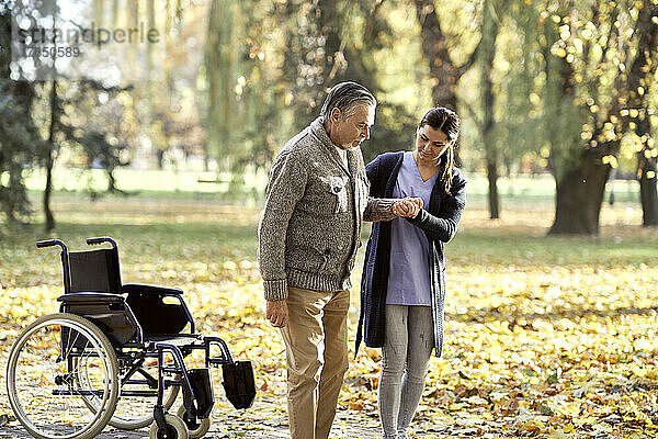 Gesundheitshelfer hilft älterem behinderten Mann beim Spazierengehen im Park