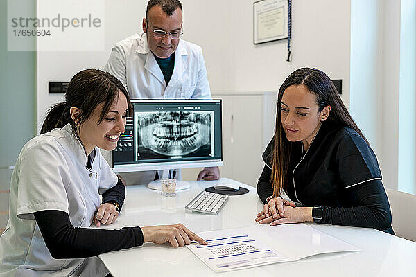 Lächelnder Zahnarzt diskutiert mit Krankenschwester über medizinischen Bericht am Schreibtisch in der Klinik