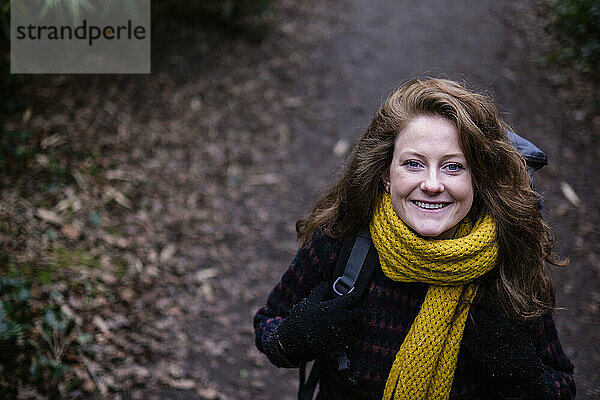 Glückliche Frau mit gelbem Schal und Rucksack im Wald