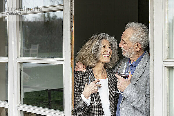 Lächelndes älteres Paar mit Weingläsern  das vor der Tür steht