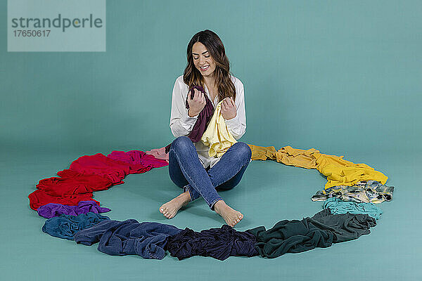 Happy woman with t-shirt sitting inside circle made of clothes against blue background