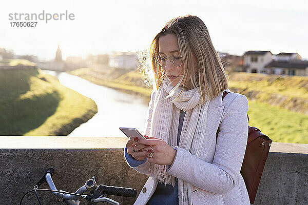 Junge Frau mit Fahrrad nutzt Mobiltelefon an sonnigem Tag