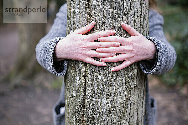 Junge Frau umarmt Baumstamm im Wald