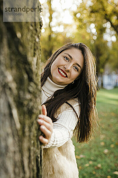 Glückliche Frau mit langen Haaren steht am Baum im öffentlichen Park
