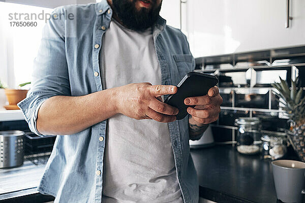 Mann benutzt Smartphone in der heimischen Küche