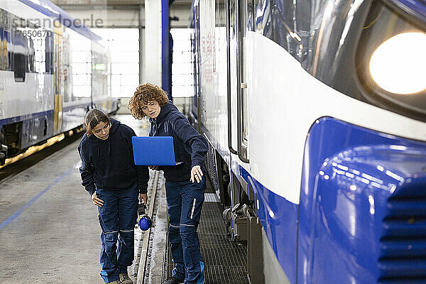 Ingenieur hält Laptop und erklärt Auszubildenden die Einschienenbahn in der Fabrik