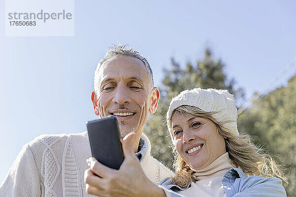 Lächelndes älteres Paar  das an einem sonnigen Tag ein Selfie über sein Smartphone macht