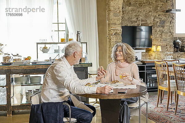 Smiling senior couple enjoying breakfast sitting at table in boutique hotel