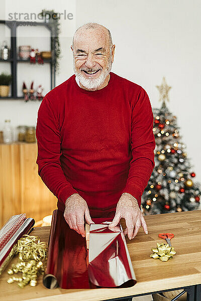 Glücklicher älterer Mann verpackt Weihnachtsgeschenk auf dem Tisch zu Hause