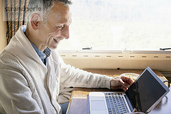 Smiling man with laptop in camper van