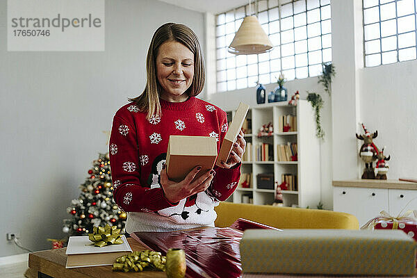 Lächelnde Frau blickt auf die Geschenkbox im Wohnzimmer