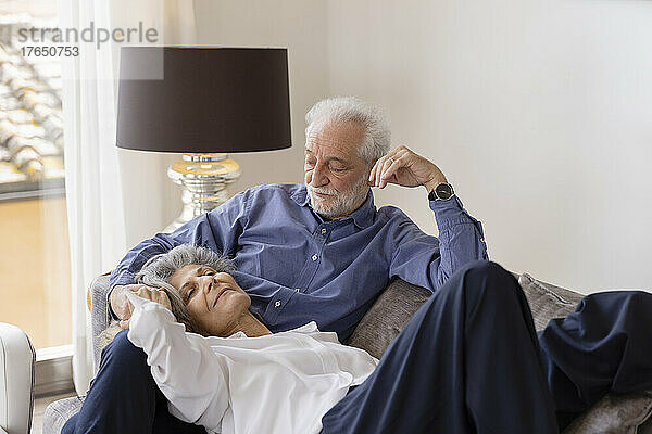 Ältere Frau liegt auf dem Schoß ihres Mannes und sitzt auf dem Sofa im Wohnzimmer
