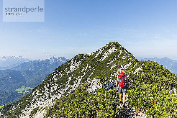 Frau mit Rucksack geht an einem sonnigen Tag auf den Berg