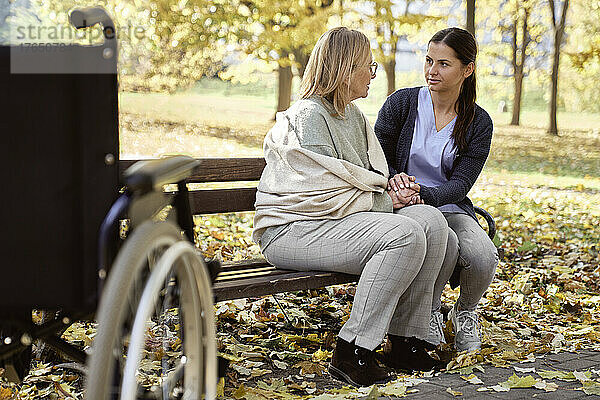 Ältere Frau spricht mit Krankenschwester  die auf Bank im Park sitzt