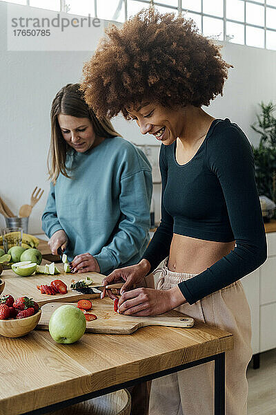Frauen schneiden Erdbeeren und Äpfel und stehen zu Hause am Tisch in der Küche