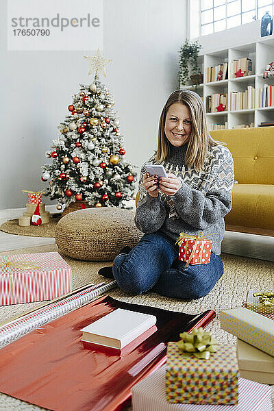 Lächelnde Frau mit Mobiltelefon und Geschenken zu Hause