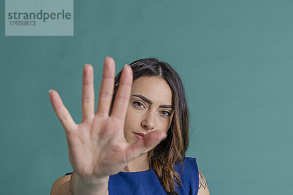 Junge Frau gestikuliert mit der Hand „Stopp“ vor blauem Hintergrund