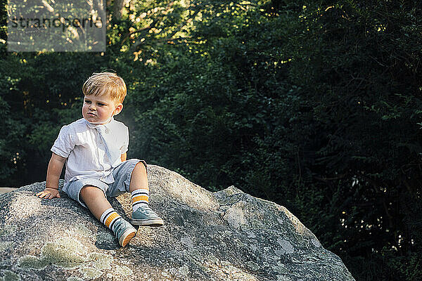 Preschool boy sitting on rock in forest