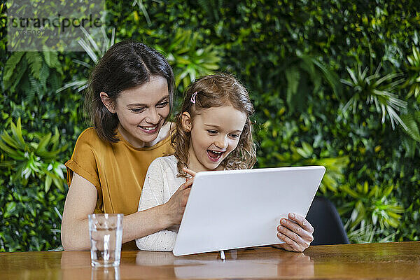 Glückliche Mutter hilft Tochter zu Hause am Tablet-PC