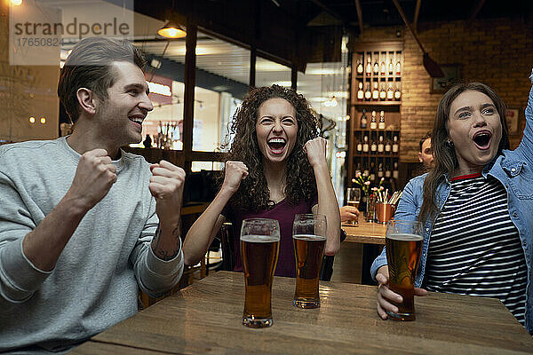 Fröhliche Fußballfans trinken Bier und schauen sich gemeinsam ein Spiel in einer Kneipe an