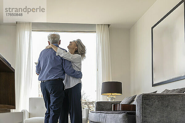 Happy senior couple dancing in living room at home