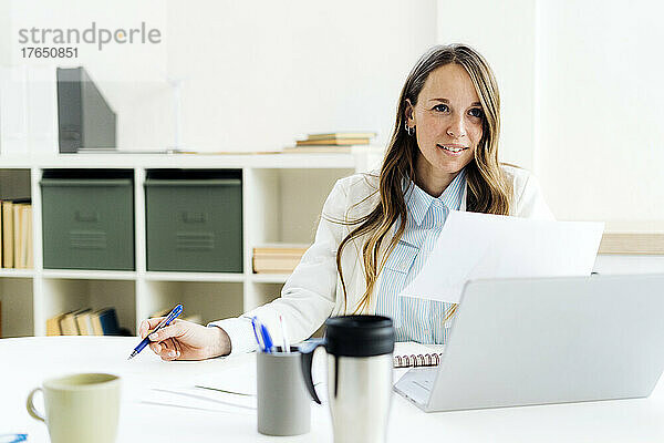 Geschäftsfrau mit Stift und Laptop am Schreibtisch
