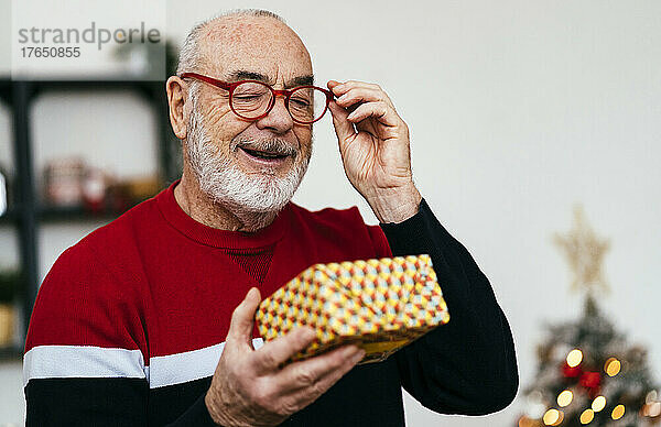 Lächelnder älterer Mann mit Brille schaut zu Hause auf die Geschenkbox