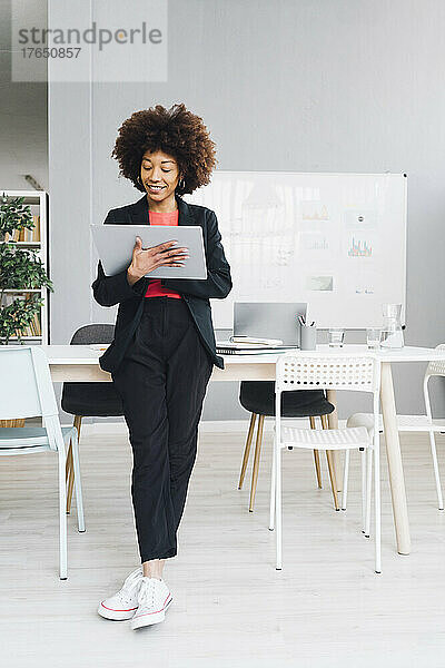 Afro-Geschäftsfrau lehnt am Schreibtisch und benutzt Tablet-PC im Büro