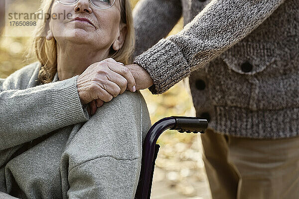 Behinderte Seniorin sitzt im Rollstuhl und tröstet Mann im Park