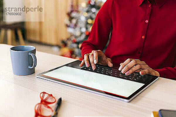 Frau tippt zu Hause am Tisch auf einem Tablet-PC