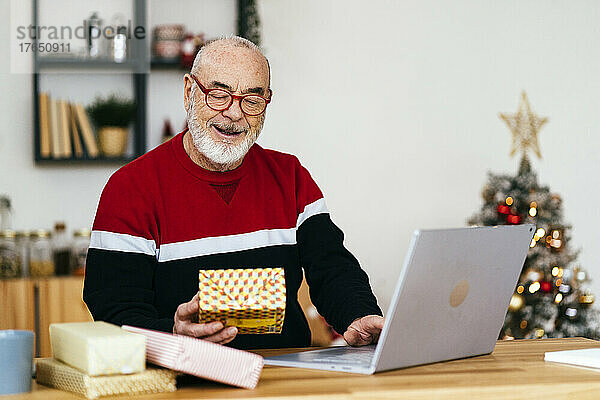 Älterer Mann hält Geschenkbox mit Laptop zu Hause in der Hand