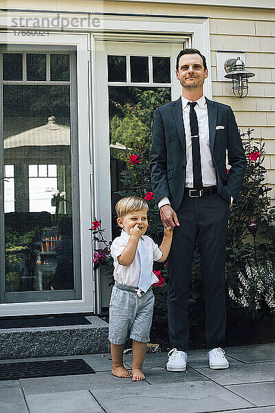 Vater und Sohn stehen Händchen haltend vor der Haustür