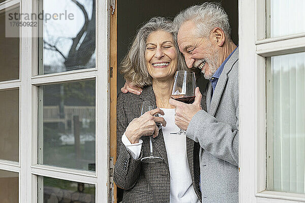 Fröhliches Seniorenpaar mit Weingläsern steht vor der Tür